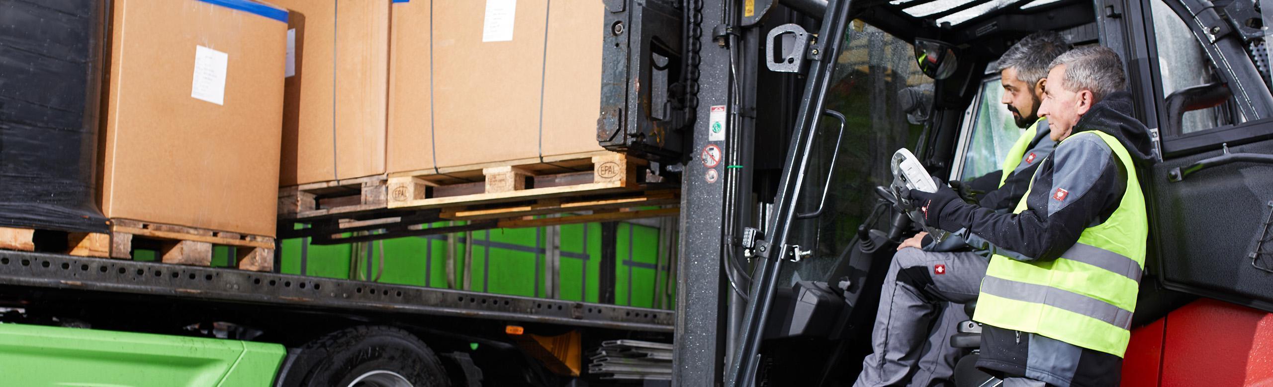 Ein Gabelstapler lädt Paletten seitlich auf einen LKW. Ein Mensch in Warnweste steht daneben. Antirutschmatte Ladungssicherung im Einsatz